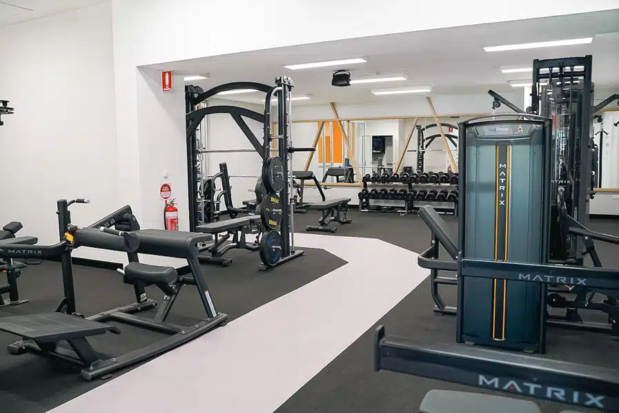Modern gym with various exercise machines, weights, and benches on black flooring.