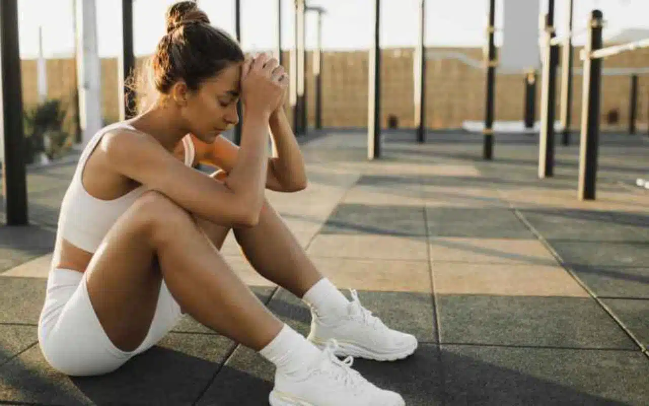 Woman in athletic wear sits on gym floor, reflecting on her gym results and progress.