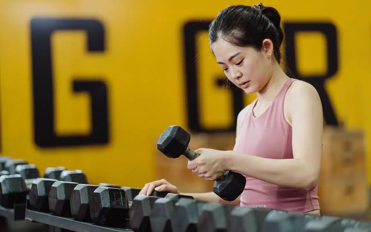Woman picking up a dumbbell at the gym, learning how to train around your menstrual cycle.